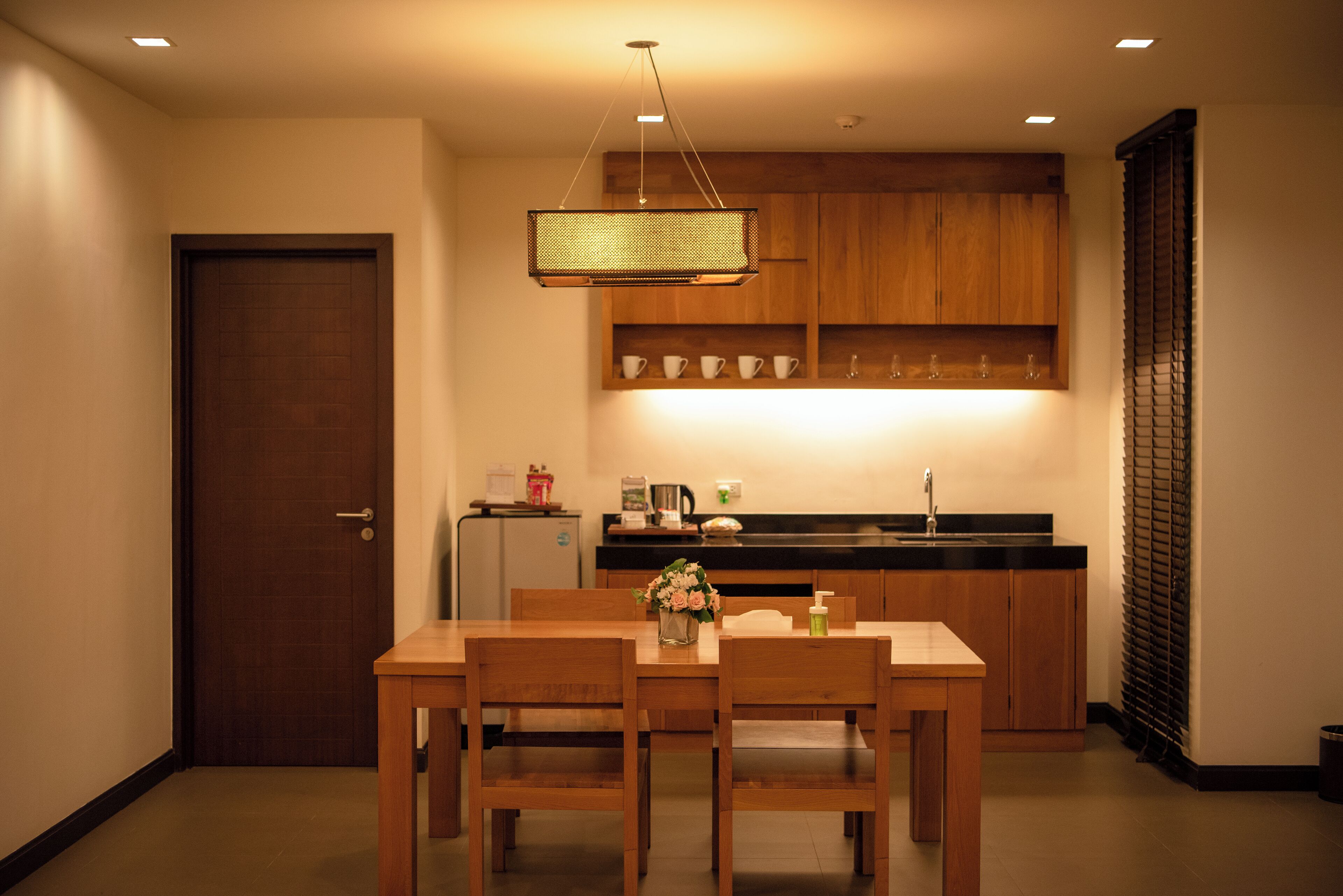 A compact kitchen with wooden cabinets, a dining table with chairs, and a hanging light fixture.