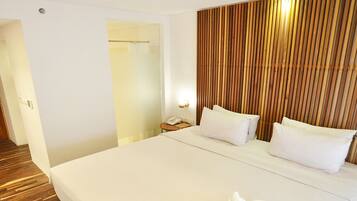 A hotel room with a large bed, a wooden headboard, a bedside table with a lamp, and a door leading to another room.
