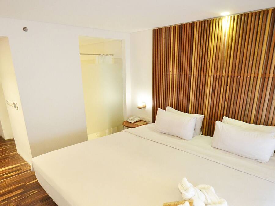 A hotel room with a large bed, a wooden headboard, a bedside table with a lamp, and a door leading to another room.