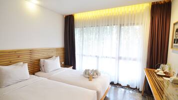 Une chambre d’hôtel avec deux lits, une tête de lit en bois, une petite table avec une chaise et une grande fenêtre avec des rideaux.