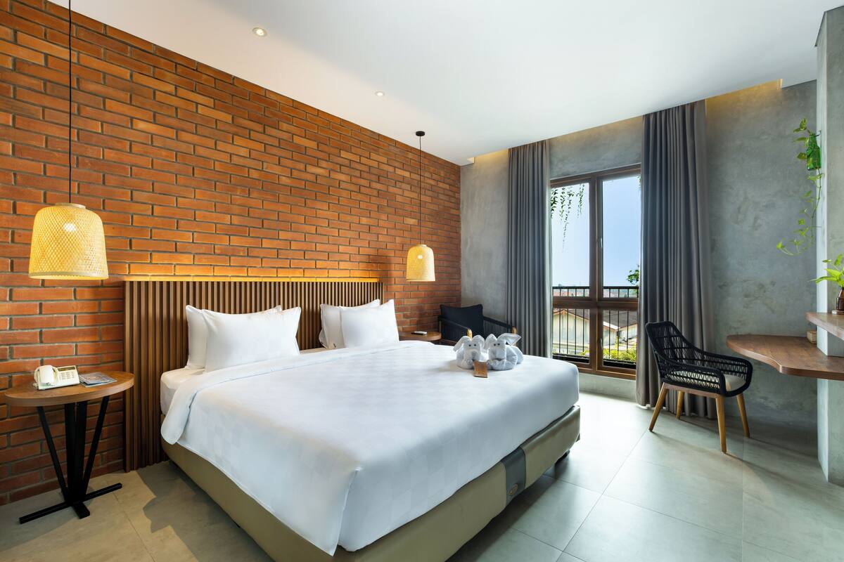 A modern hotel room with a brick wall, a large bed, a desk, and a chair.