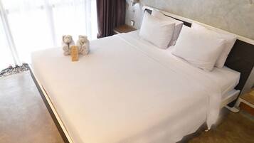 A hotel room with a large bed, a nightstand, a lamp, and a view of the outdoors.