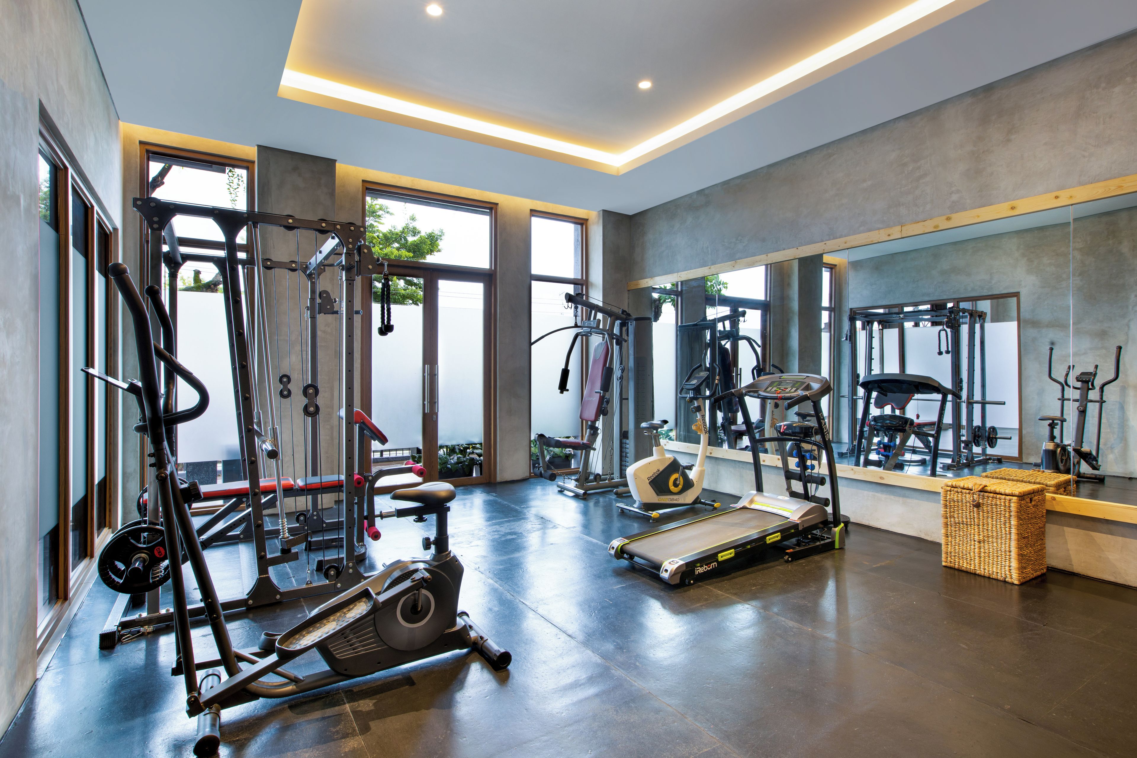Une salle de sport moderne équipée de divers appareils d’exercice, dotée de grandes fenêtres et d’un mur entièrement recouvert de miroirs.