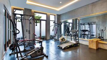 Une salle de sport moderne équipée de divers appareils d’exercice, dotée de grandes fenêtres et d’un mur entièrement recouvert de miroirs.