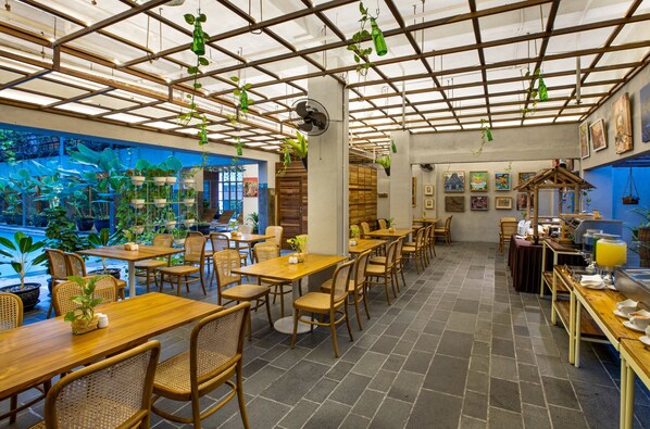 Un restaurante con mesas y sillas de madera, plantas colgantes y vistas a un jardín a través de un muro de cristal.