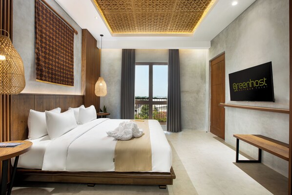 Una habitación de hotel moderna con una cama grande, un televisor montado en la pared y vistas al exterior por la ventana.