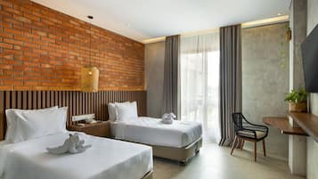 A hotel room with two beds, a desk, a chair, a TV, and a plant.