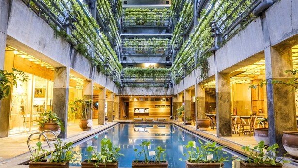 An indoor swimming pool with a central walkway, surrounded by potted plants and modern architecture. - Greenhost Boutique Hotel (Yogyakarta)