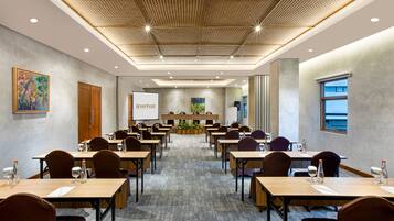 A conference room with tables, chairs, a projector screen, and a large window.
