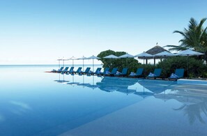 Relax by the oceanfront pool surrounded by lush greenery and a thatched-roof structure.