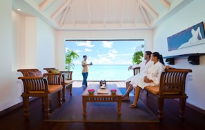 Ein Zimmer mit einer Sitzecke mit Holzbank, einem kleinen Tisch mit einem Buch und einer BlumenSchale, und Blick aufs Meer.