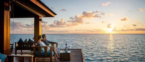 A couple on a wooden deck overlooking the sea at sunset.