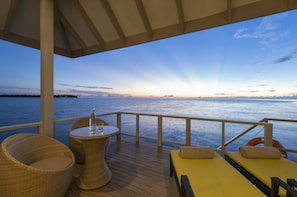 Relax on the oceanfront deck with a clear view of the distant shoreline, featuring wicker chairs and a small table.