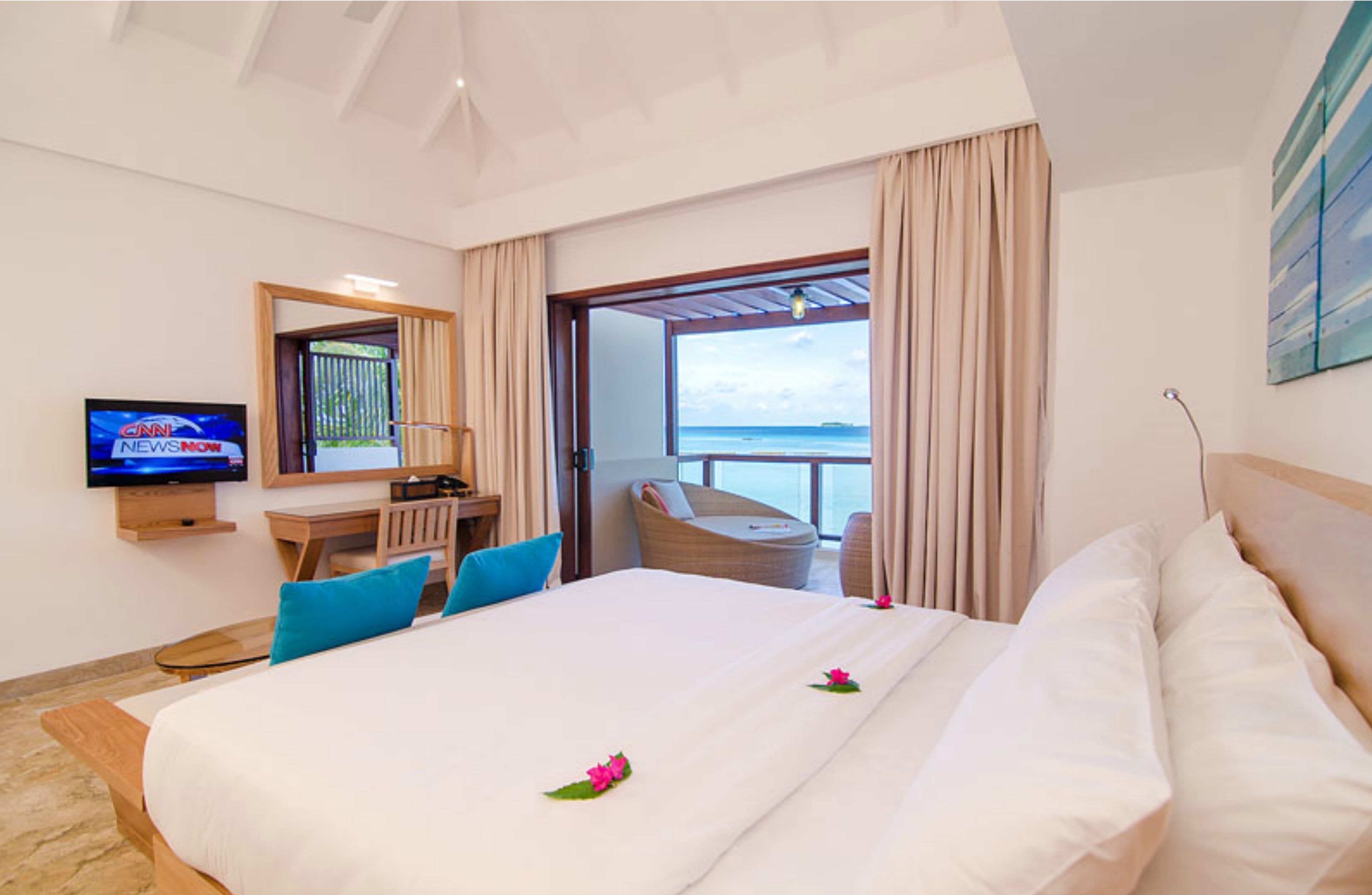A hotel room with a bed, a desk with a chair, a television, and a view of the ocean.