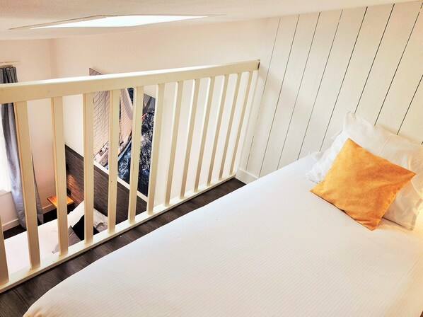 Un dormitorio con una cama blanca, cabecera de madera y vistas a un balcón.