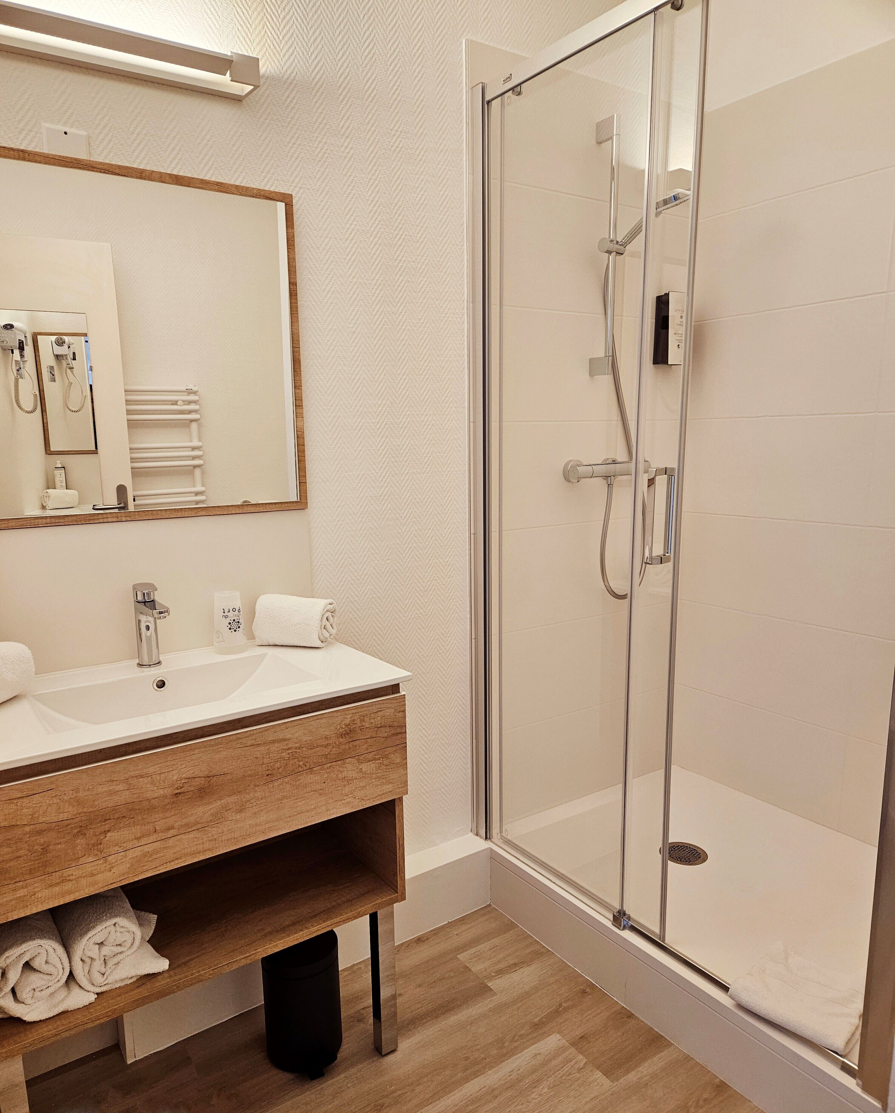 A modern bathroom with a wooden vanity, a glass shower enclosure, and a large mirror.