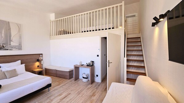 A bedroom with a bed, bedside table, nightstand, and a small desk with a chair. There is a lofted sleeping area above the bed. - Hotel Du Port (Saint-Martin-de-Re)
