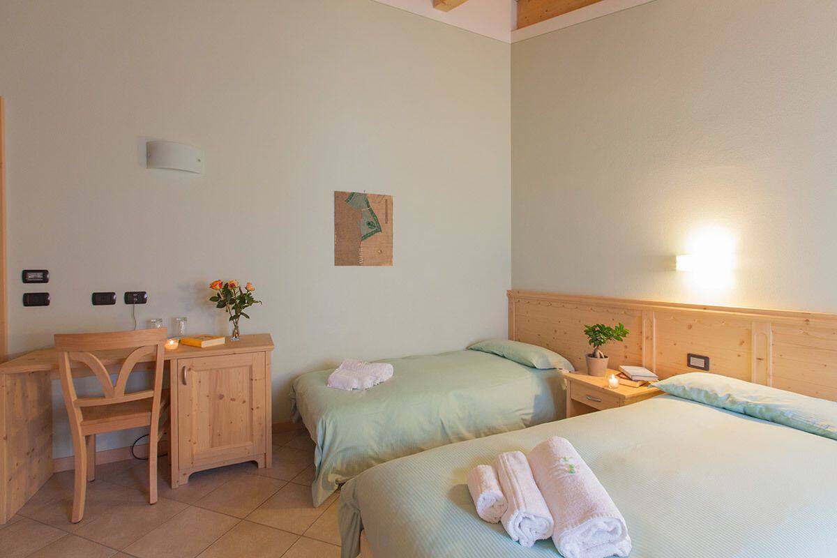 Habitación de hotel con dos camas, un escritorio de madera, una silla, una mesita con una planta y una lámpara fijada a la pared.