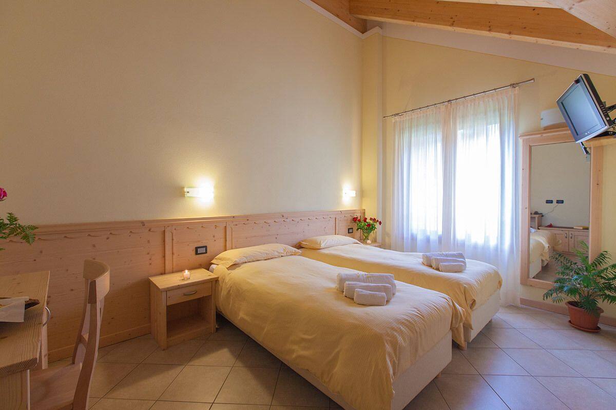 Habitación de hotel con dos camas, un escritorio, una silla, un televisor montado en la pared y una planta en maceta.