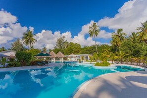 Una piscina azul cristalina rodeada de palmeras y construcciones con techo de paja.