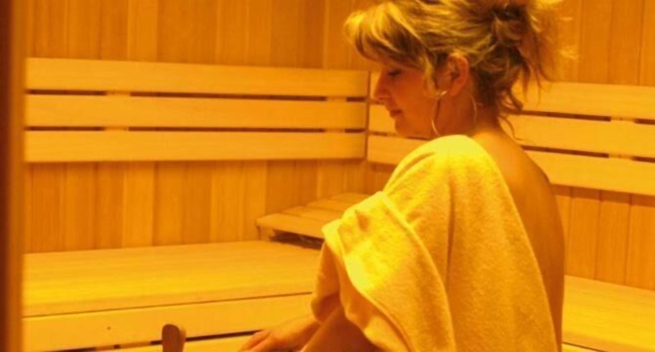 Une personne est assise sur un banc en bois dans une pièce dont les murs et les bancs sont également en bois.