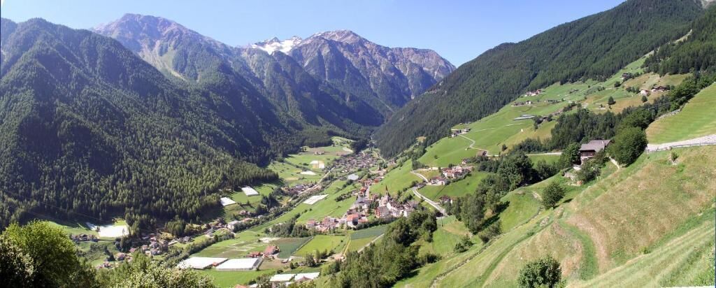 Un valle con un pequeño pueblo ubicado entre montañas, con casas y edificios dispersos por el paisaje.