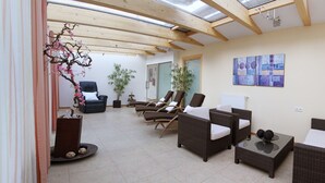 Una stanza spaziosa con soffitto alto, travi in legno e un lucernario. Sono presenti diverse poltrone in vimini e un divano, disposti per il relax.