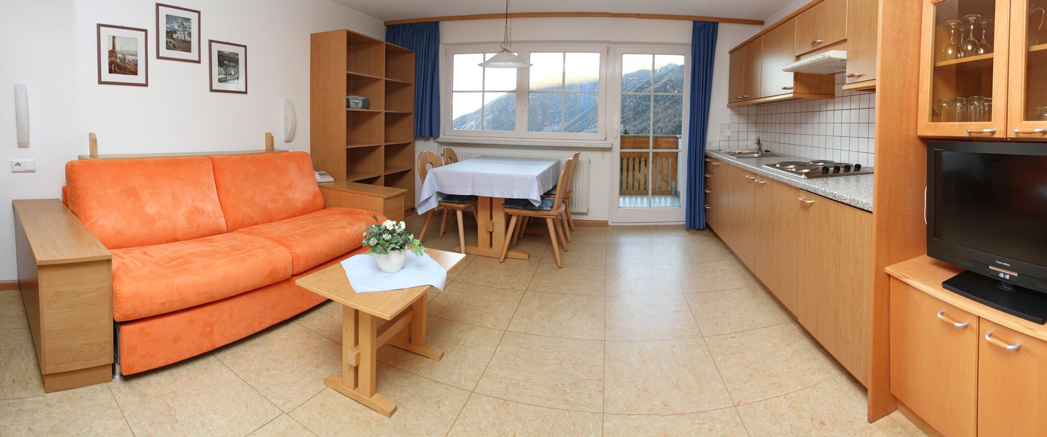 Un espacio habitable compacto con sofá, mesa de comedor, zona de cocina y televisor.