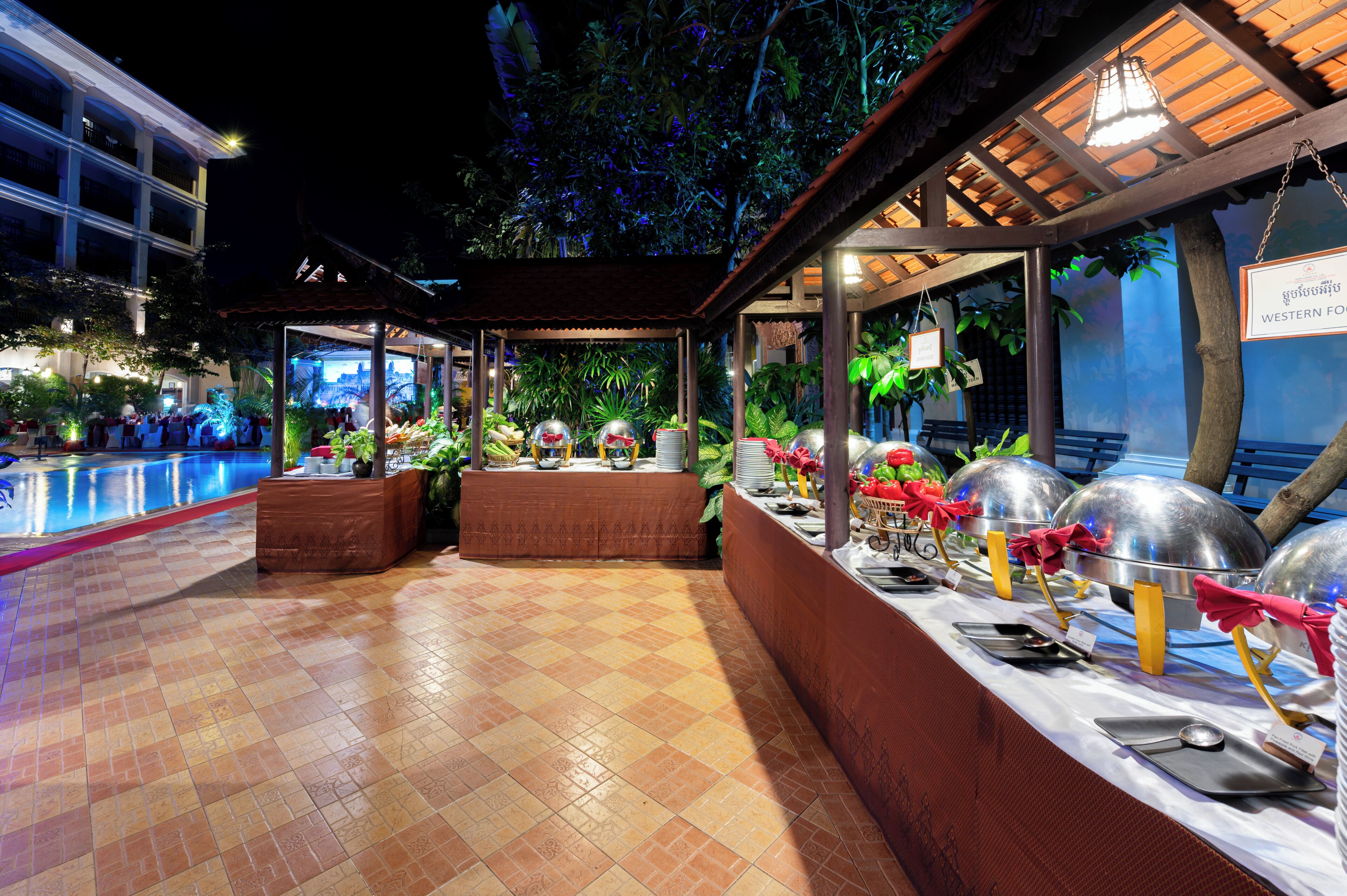 An outdoor dining area with a pool, covered seating, and a buffet setup.