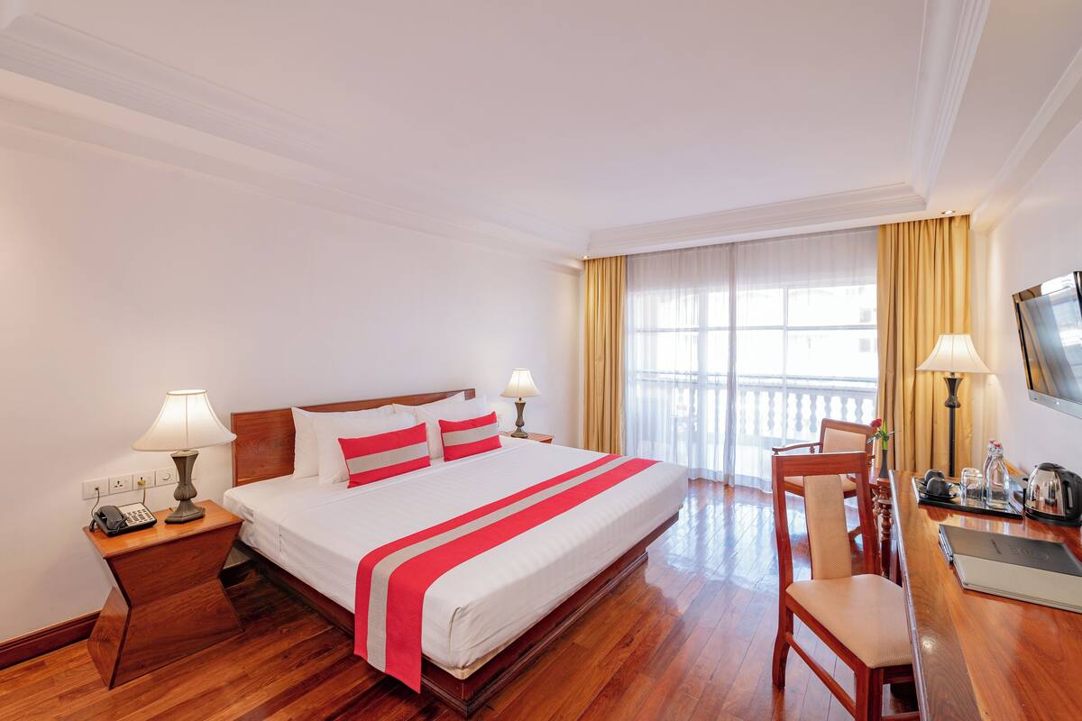 A hotel room with a large bed, bedside lamps, a desk with a chair, and a television.