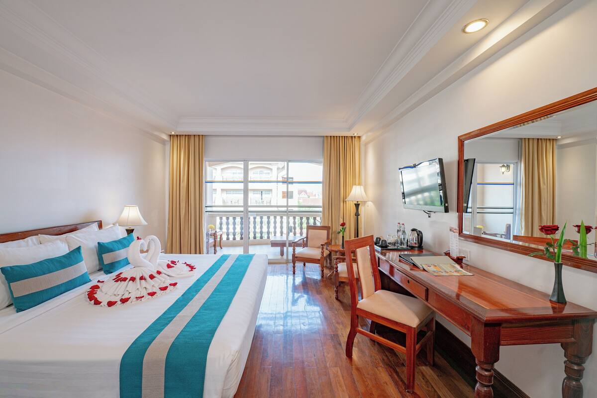 A hotel room with a large bed, a desk, a chair, a television, and a window with curtains.