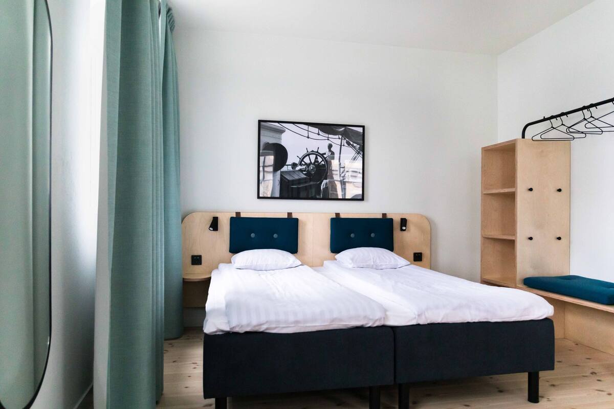 A double bed with a headboard, a wooden wardrobe, and a framed picture on the wall.