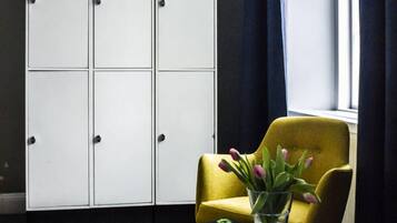 A corner room with a yellow armchair, a small table with a book and a vase of flowers, and a white wardrobe against a dark wall.