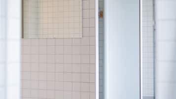 Un baño con paredes y suelo de azulejos blancos, un espejo y una puerta que conduce a otra habitación.