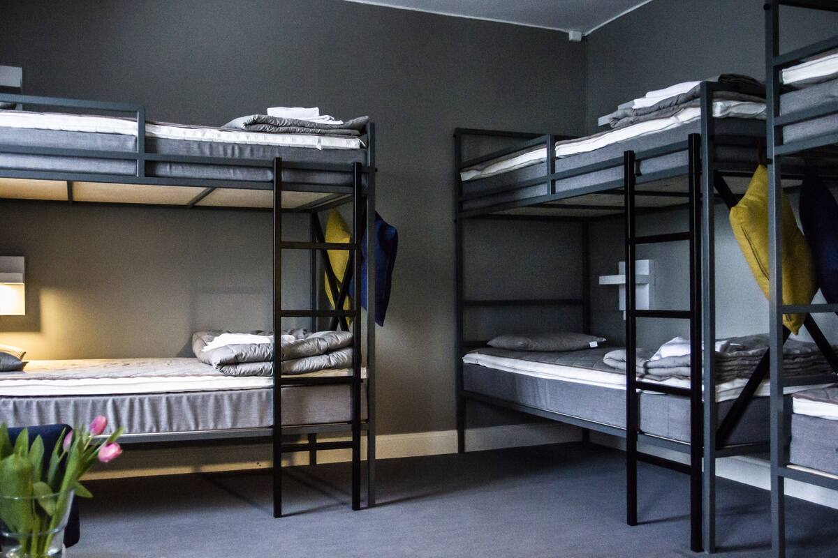 A dormitory room with bunk beds, a bedside table, and a lamp.