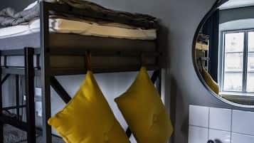 A bunk bed with folded blankets and pillows, a round mirror, and a view of a cityscape through a window.