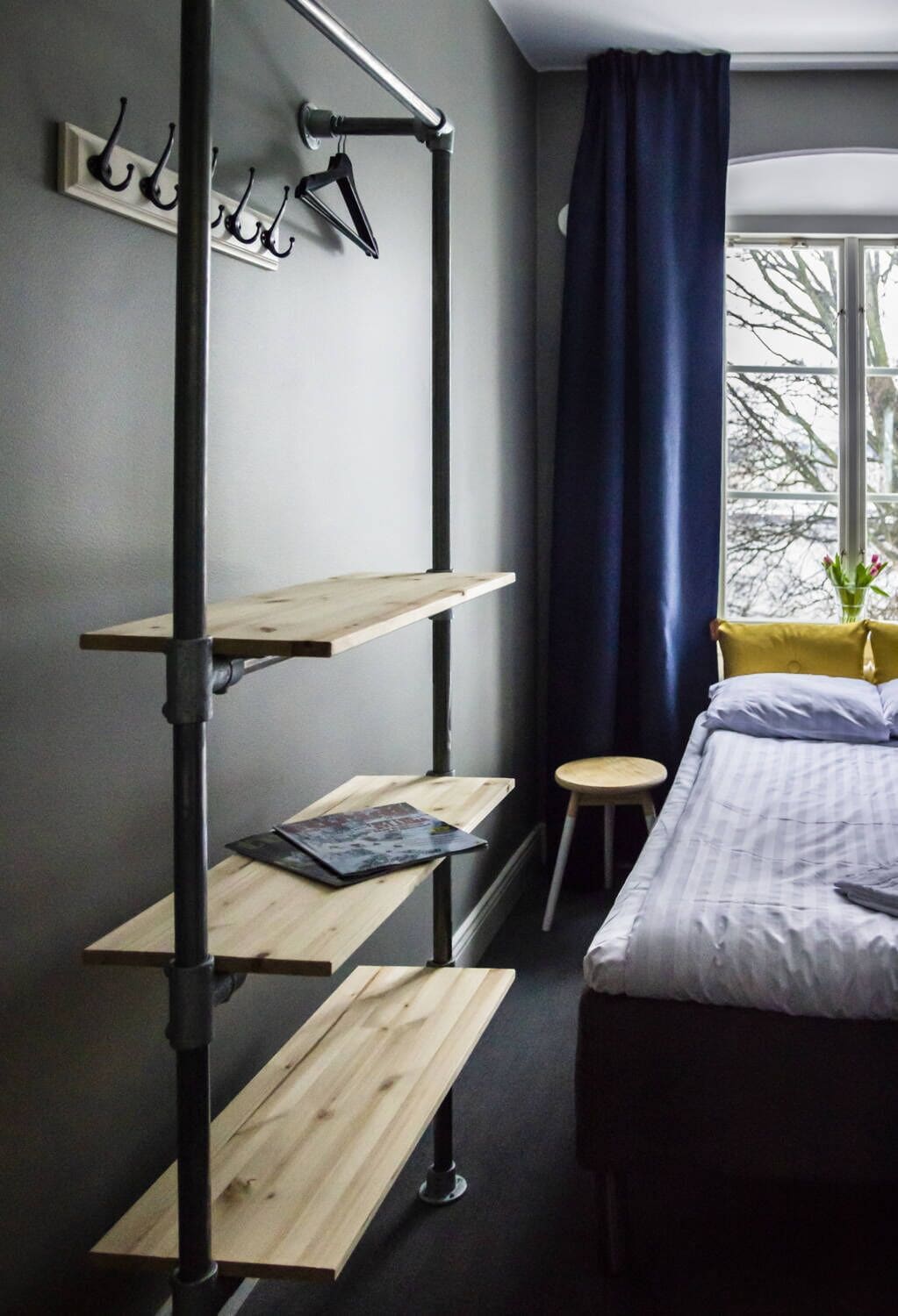 A room with a bunk bed, a desk with a laptop, a chair, a window with curtains, and a wall-mounted coat rack.