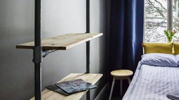 A room with a bunk bed, a desk with a laptop, a chair, a window with curtains, and a wall-mounted coat rack.