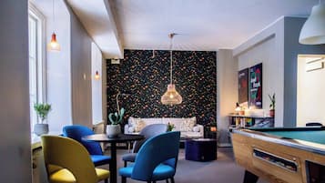 Un salon moderne avec une table de billard, des chaises bleues et jaunes, une table ronde et un mur noir orné de motifs colorés.
