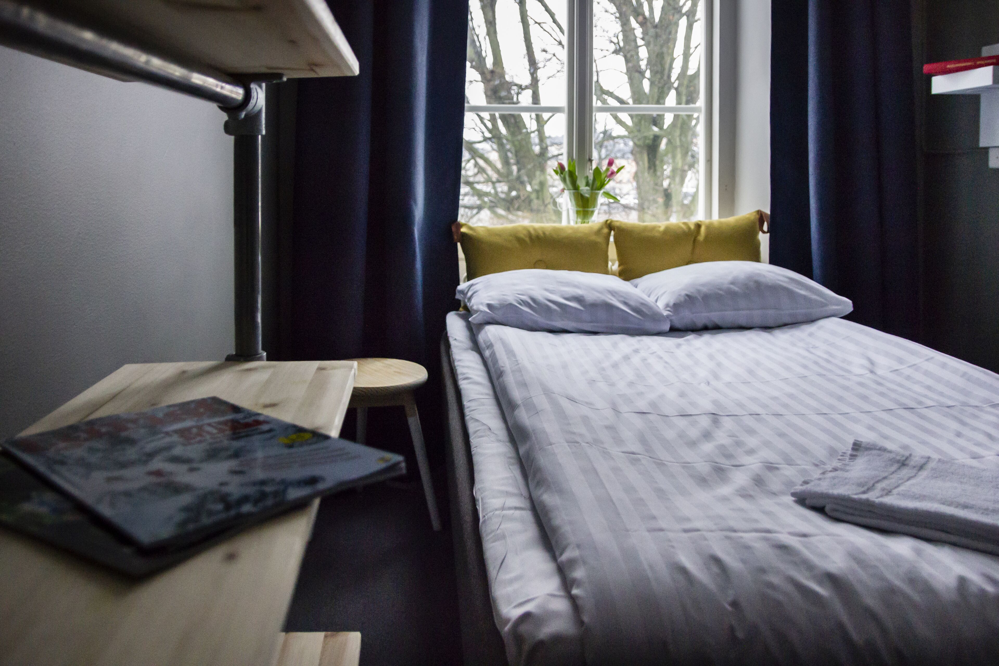 Habitación de hotel con cama, una mesita, una silla y ventana con vista a árboles.