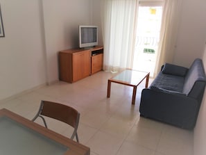 A living room with a sofa, a coffee table, a TV on a wooden cabinet, and a chair.