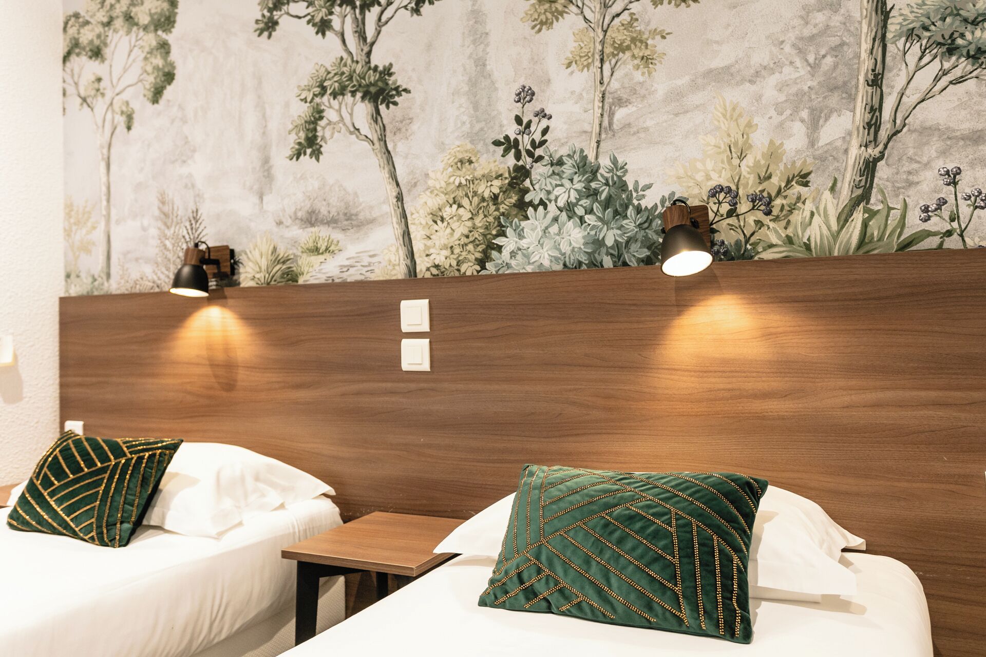 Een hotelkamer met twee bedden, elk voorzien van een kussen, een houten hoofdbord en een muurschildering van bomen en planten.