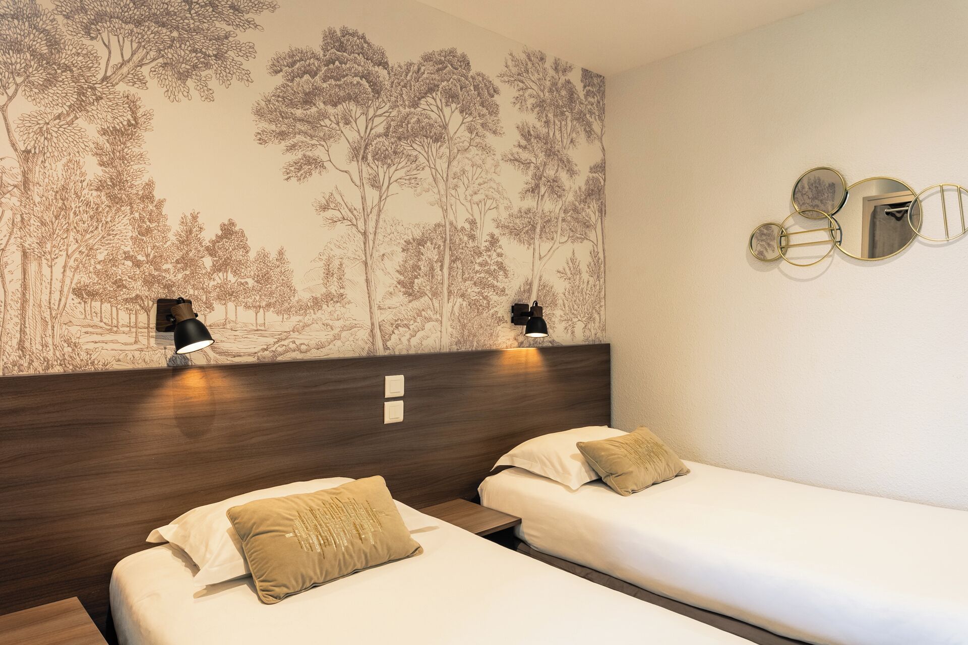 Habitación de hotel con dos camas individuales, cabecero de madera, lámpara de pared y un mural decorativo con un árbol.