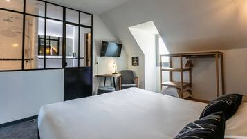 A modern hotel room with a large bed, a desk, a chair, a TV, and a wardrobe.