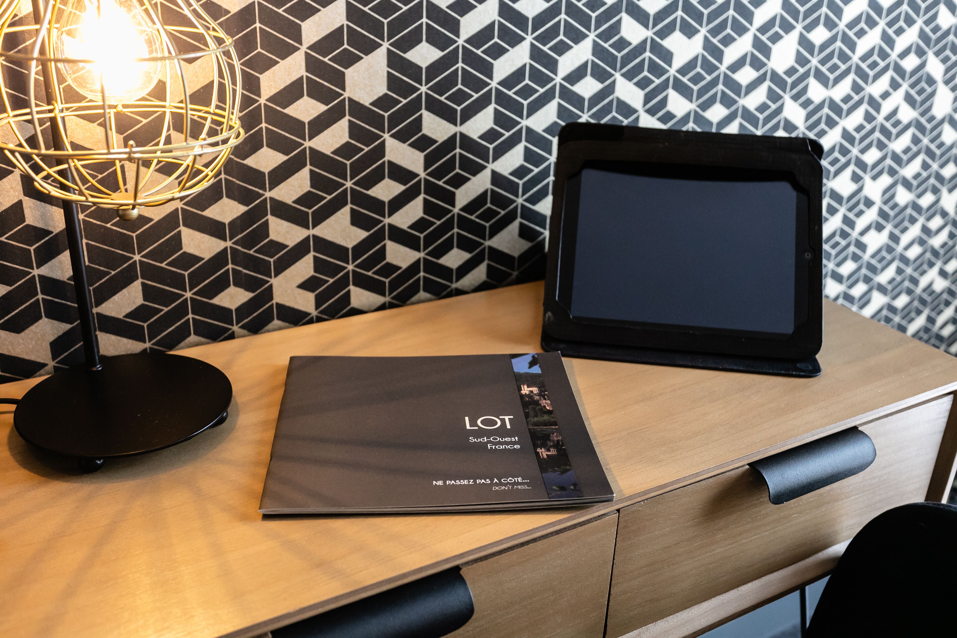 A wooden desk with a laptop, a tablet, and a lamp.