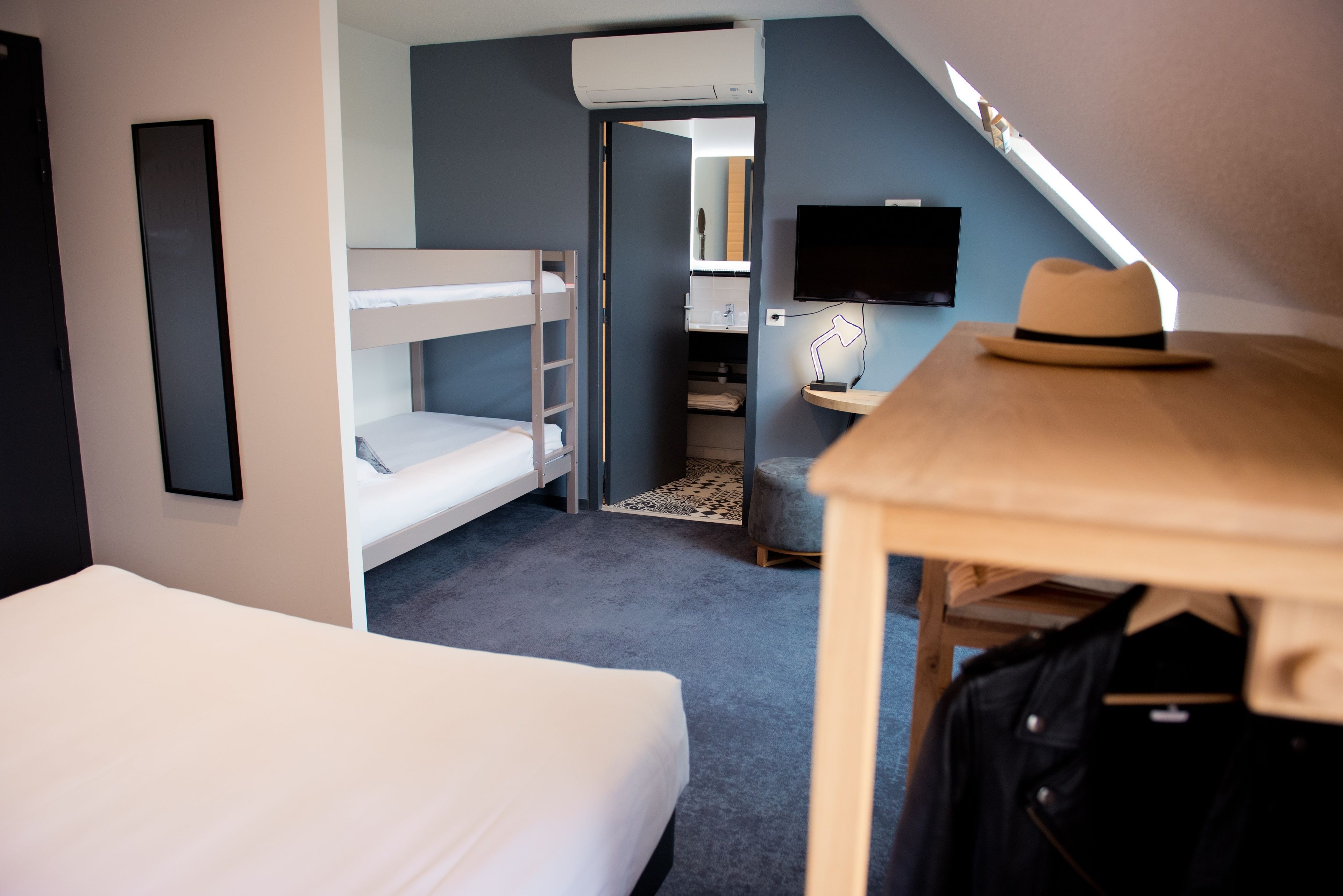 A hotel room with bunk beds, a desk with a hat, a TV, and an air conditioning unit.