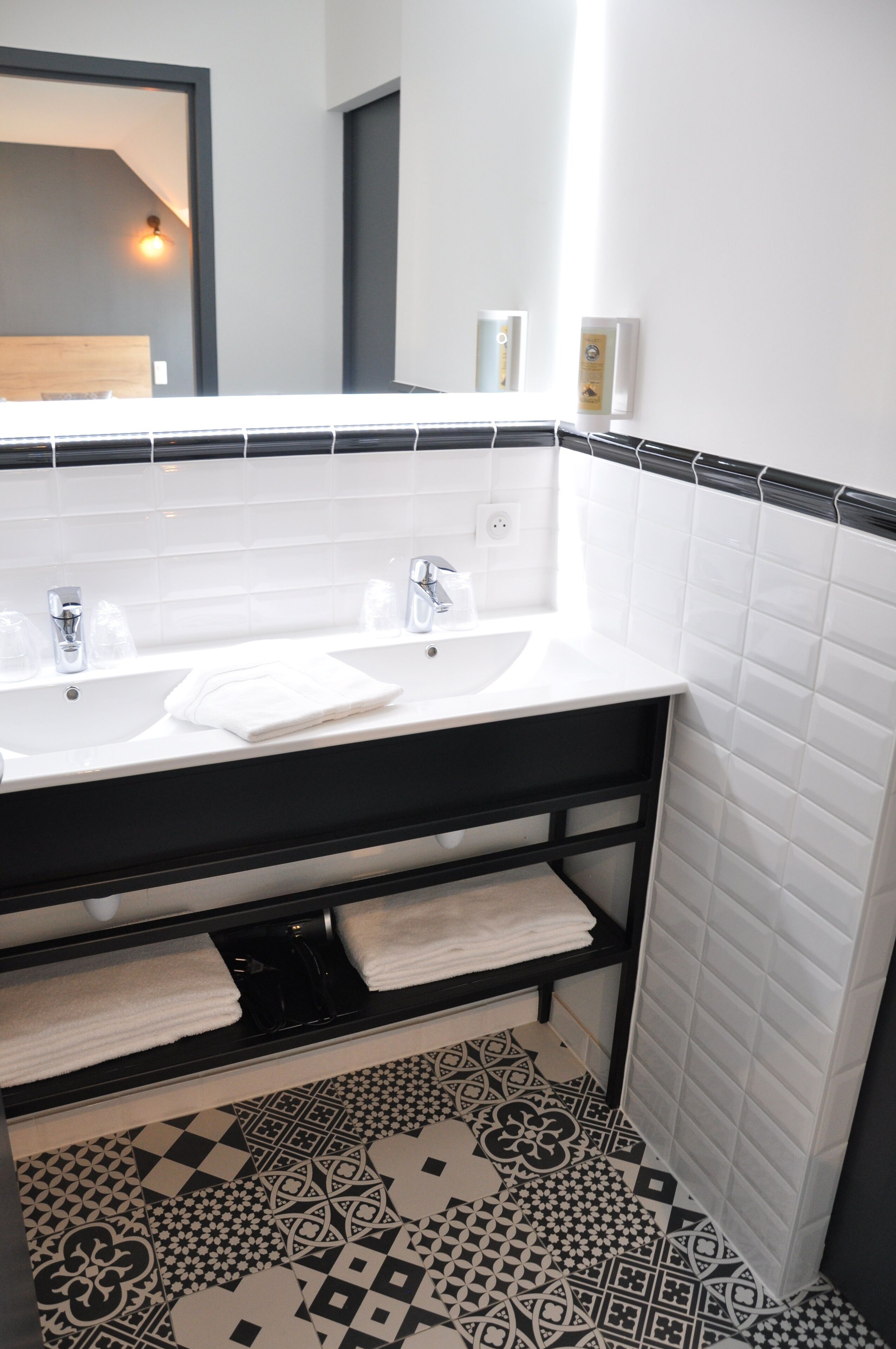 Un baño con lavamanos blanco, encimera negra y baldosas de suelo con estampado.