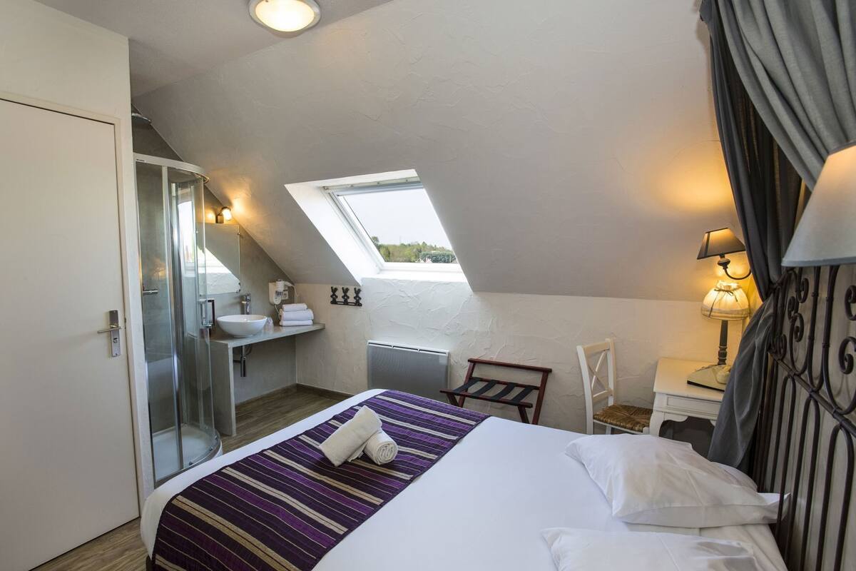 A bedroom with a bed, a window, a bathroom, and a desk.