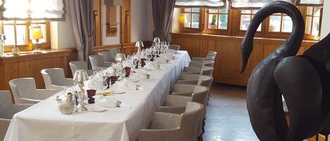 A long dining table set for a meal, wooden beams on the ceiling, and a large black sculpture of a swan.