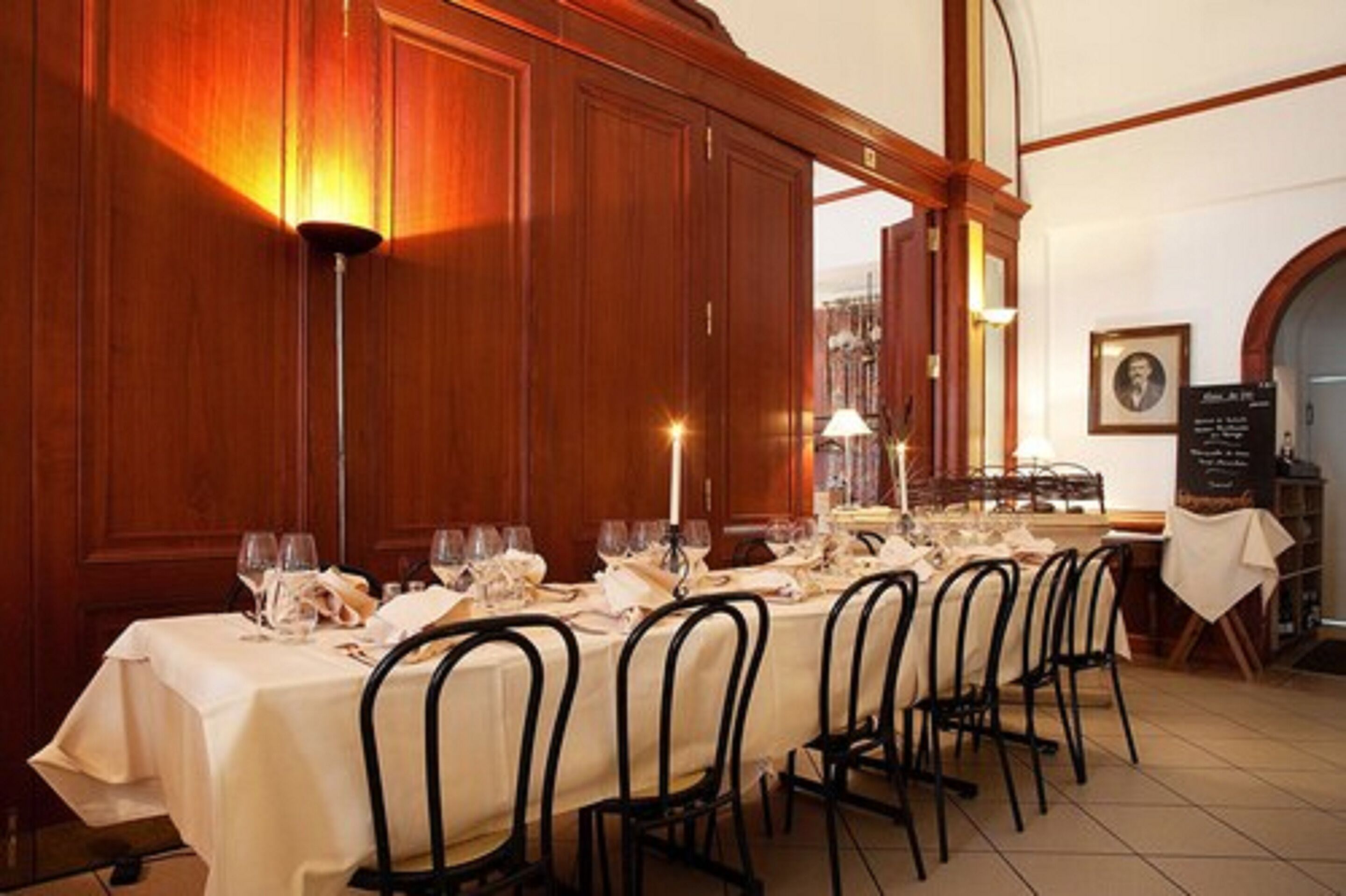 A dining area with a long table set for a meal, wooden paneling on the walls, and a framed picture on the wall.